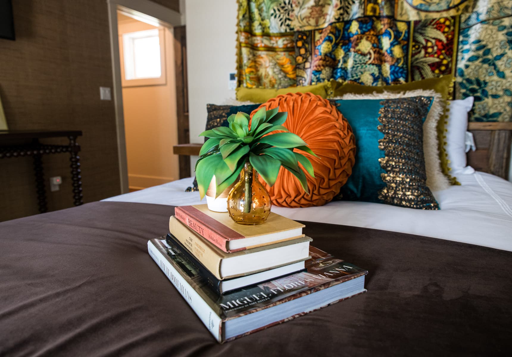 A stack of books and a small vase with a plant on a queen bed