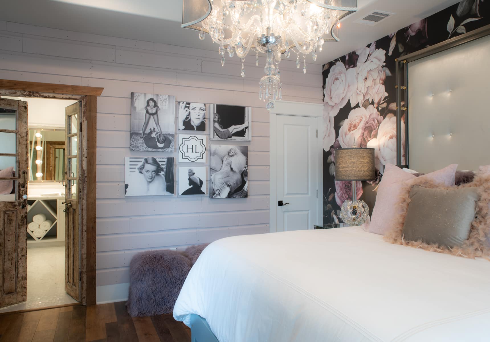 King bed in a room with floral decorative wall paper a chandelier and a wooden double door to a bathroom