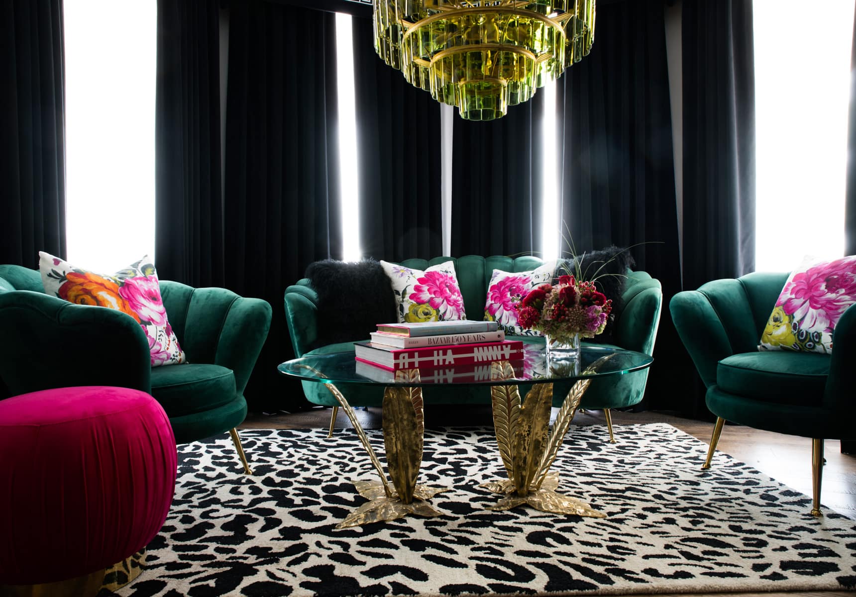 Seating area for 5 with a glass table on a animal print area rug with a green glass chandelier and dark ceiling to floor curtains