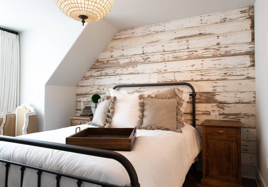 Queen bed in a room with a rustic wood plank wall and seating area near a window