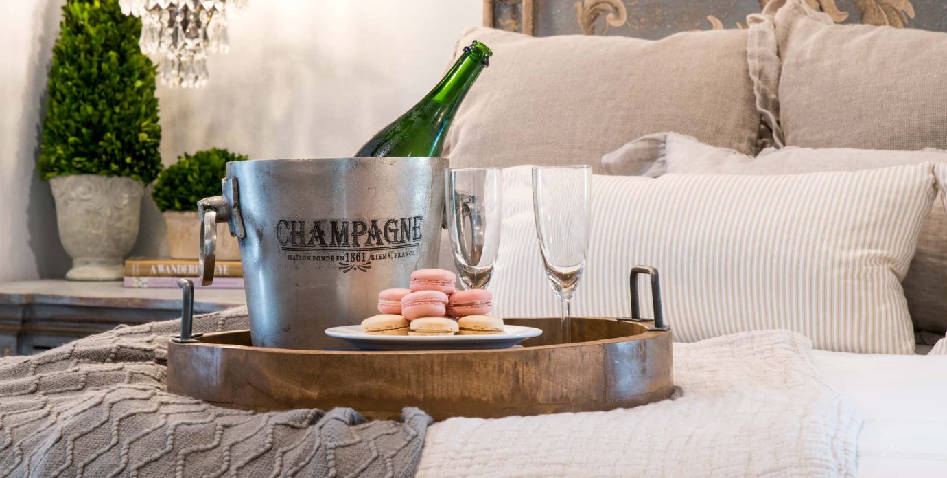 Bottle of Champagne and macrons on a tray on a bed