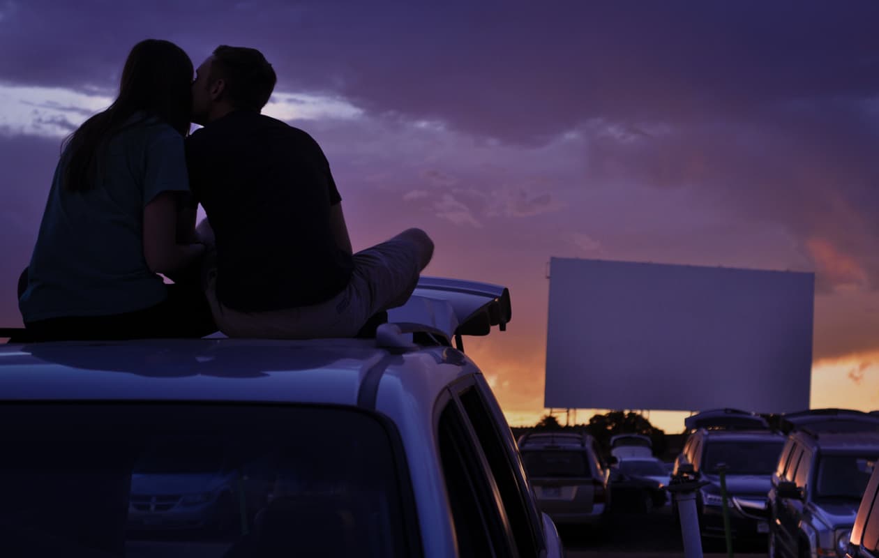 A couple sitting on the roof of their car at a drive-in theater